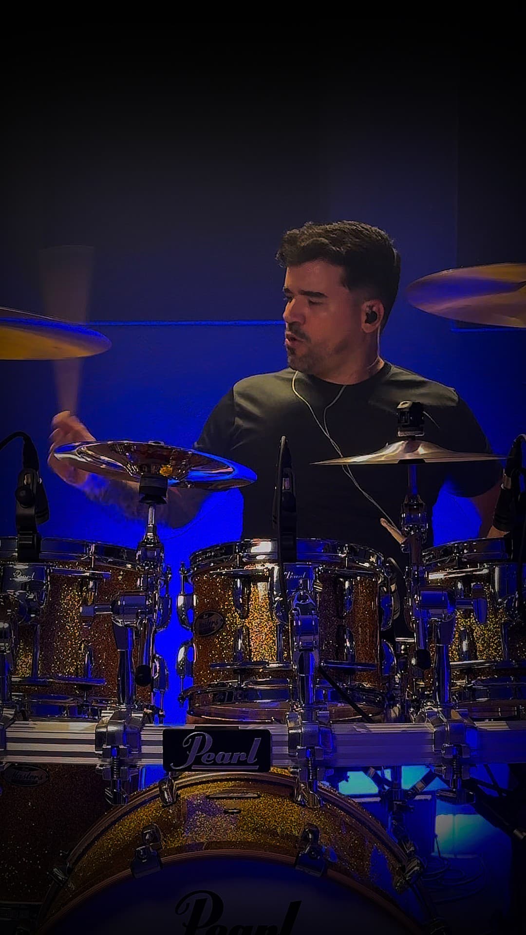 Marco Drums tocando bateria durante a gravação de um drum cover, sob luz azul